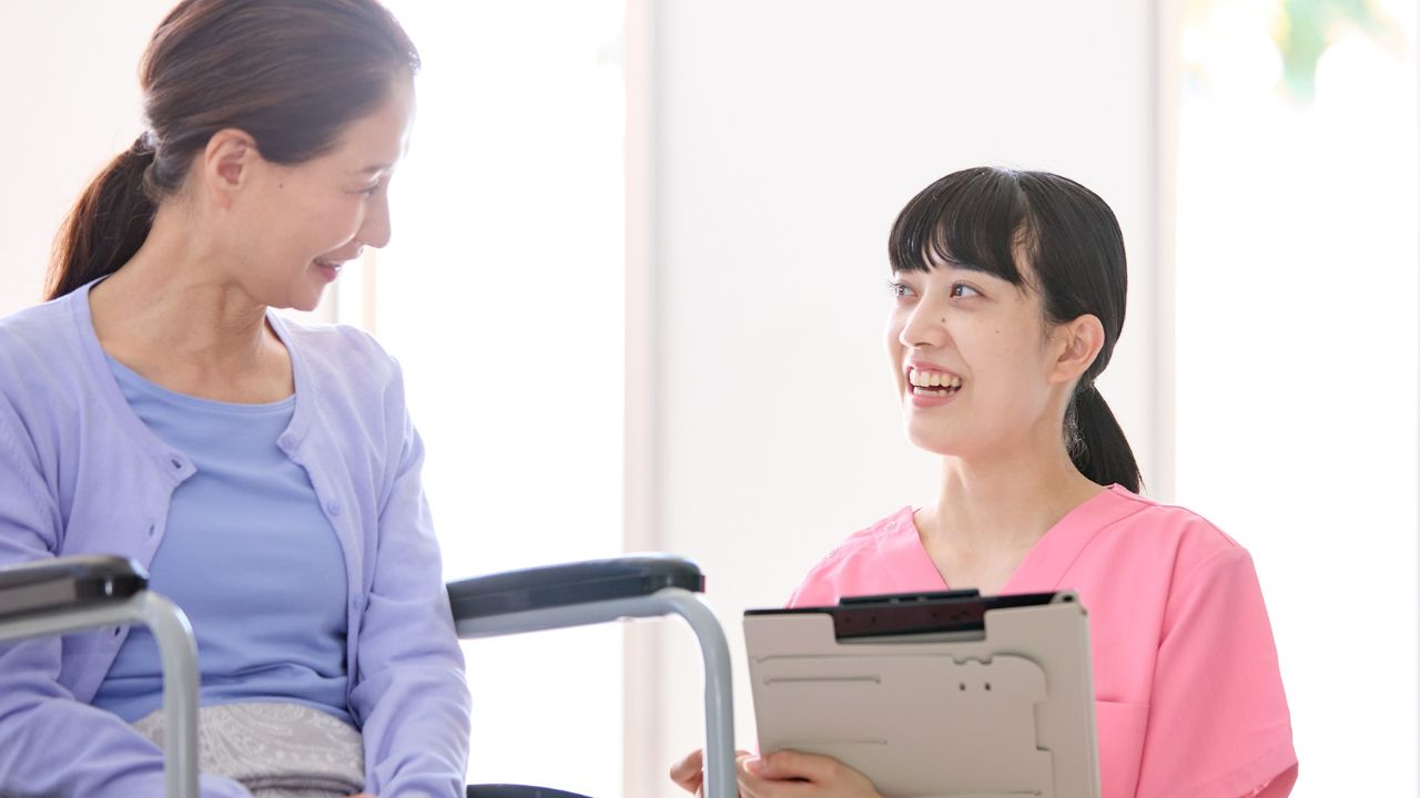 車いすに乗った高齢女性と会話をしている介護士