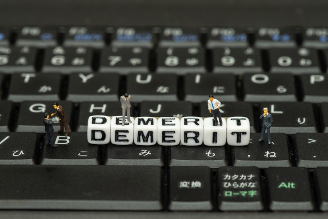 キーボードの上に置かれたMeri Demeritと書かれた文字とミニチュアのビジネスマン人形