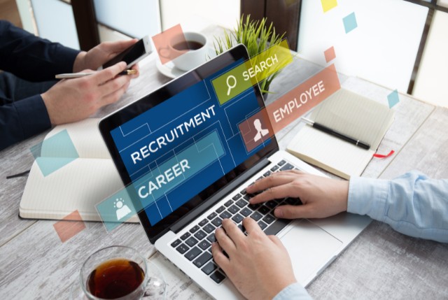 ノートパソコンの画面に『RECRUITMENT』『CAREER』『SEARCH』『EMPLOYEE』といった採用関連キーワードが表示され、人材紹介ビジネスシーンのイメージ