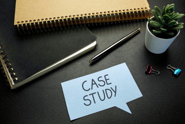 黒いデスクの上にノートやペン、観葉植物が置かれ、中央に『CASE STUDY』と書かれた紙が置かれているビジネス学習や分析のイメージ
