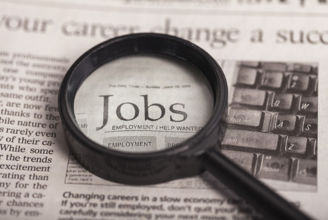 新聞の求人欄「Jobs」を虫眼鏡で拡大している様子。求人情報の検索や人材募集を象徴するイメージ。