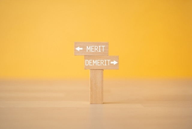 木製の看板に「MERIT」と「DEMERIT」の矢印が描かれたイメージ。採用活動や外国人雇用のメリット・デメリット比較を象徴。
