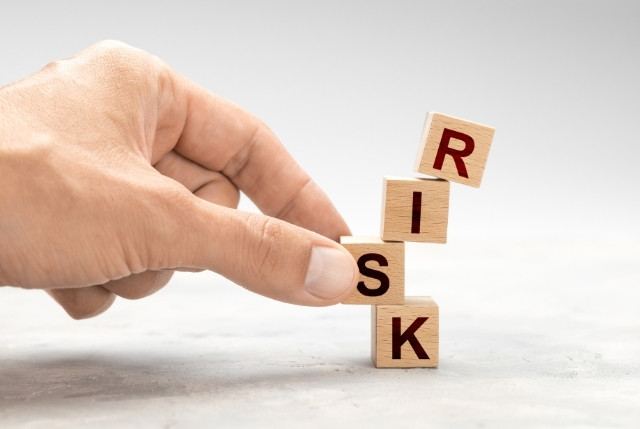 「RISK」と書かれた積み木を指で支える手。企業経営や採用活動におけるリスク管理と意思決定を象徴するイメージ。