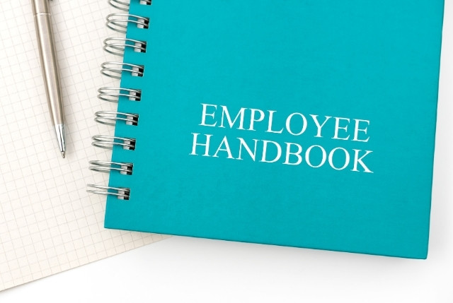 青い表紙に「EMPLOYEE HANDBOOK」と書かれた社員ハンドブック。外国人材の就業ルールや社内制度の説明書。