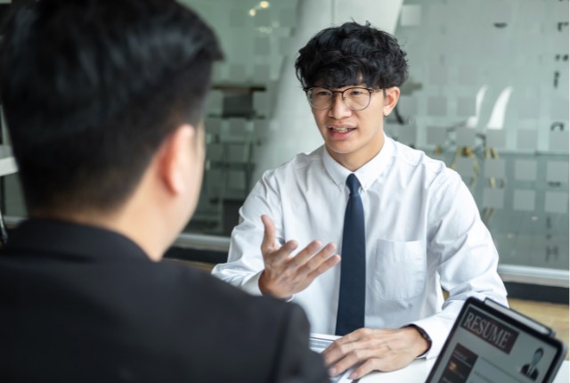 定期面談で話す外国人男性と受け入れ企業担当者。特定技能外国人の支援サポートのひとつでもある面談を行う様子を表すビジネスシーン。