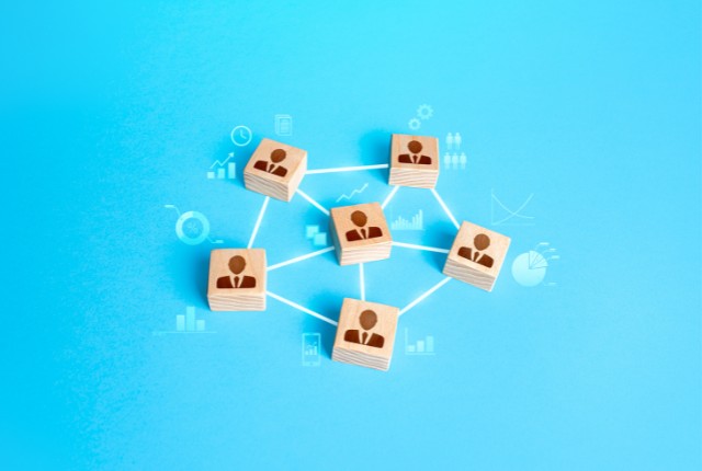 青い背景に木製ブロックで人のアイコンが描かれ、線でつながれたネットワーク構造。特定技能外国人の支援連携を象徴。