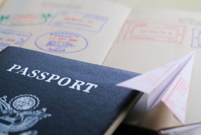 パスポートと出入国スタンプ帳、紙飛行機の画像。海外渡航やビザ取得、特定技能外国人の入国手続きを表現。