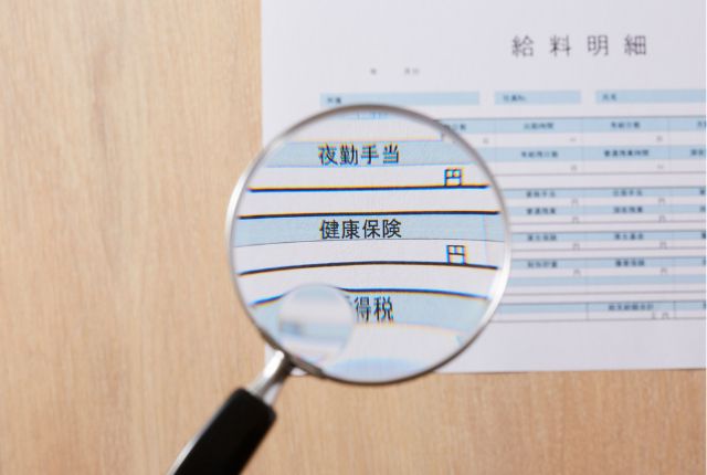 拡大鏡で給与明細の「健康保険」や「夜勤手当」などを確認している様子。特定技能外国人の給料管理解説用イメージ。