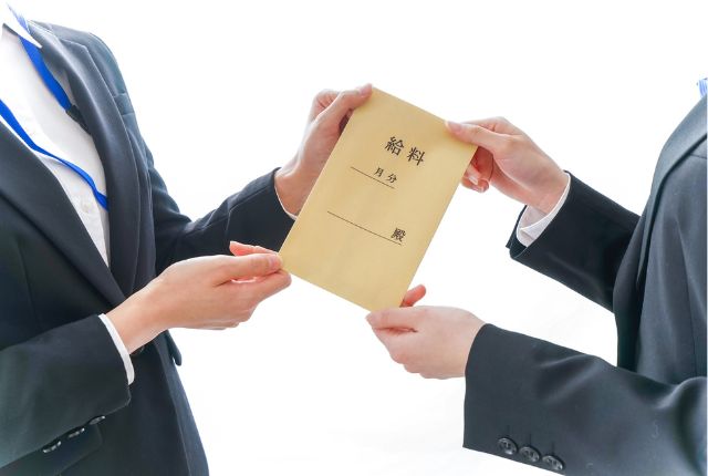 スーツ姿の人物が「給与」と書かれた封筒を受け渡す様子。特定技能外国人の給料支給や雇用管理のイメージ