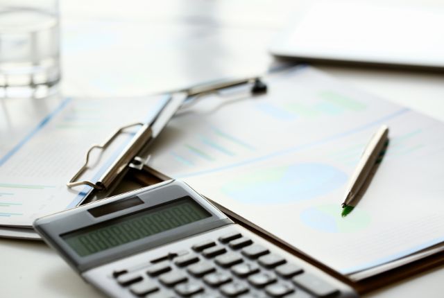 電卓とグラフ入りの資料、ペンが置かれたデスク。特定技能外国人の給与計算や労務管理をイメージした写真