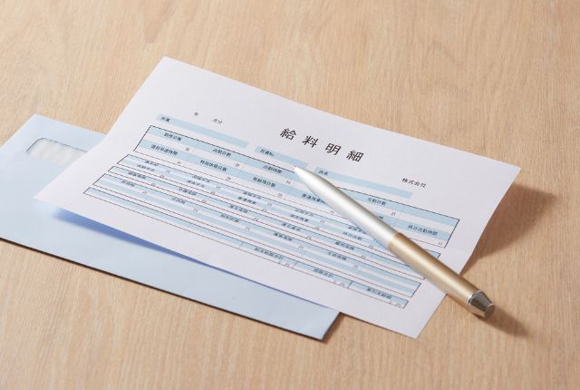 机の上に置かれた給与明細書とペン。外国人労働者の雇用管理や給与計算に関する実務を示すイメージ。