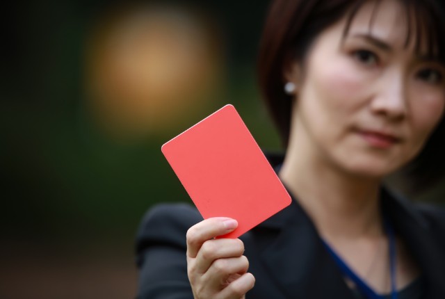 女性がレッドカードを掲げる様子。特定技能外国人の失踪や違反に対するペナルティを示すイメージ