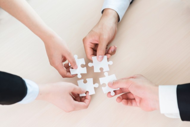 4人の手がパズルを組み合わせる様子。特定技能外国人支援における企業・支援機関の連携を表すイメージ